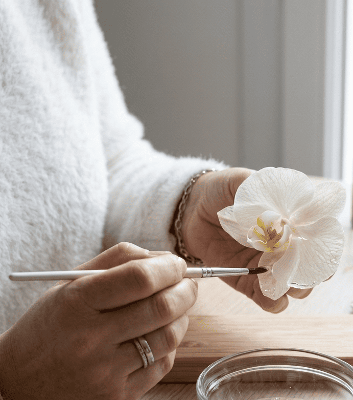 L'artisane AnneFicelle appliquant délicatement de la résine UV au pinceau sur une véritable orchidée Mado dans son atelier en Bretagne.