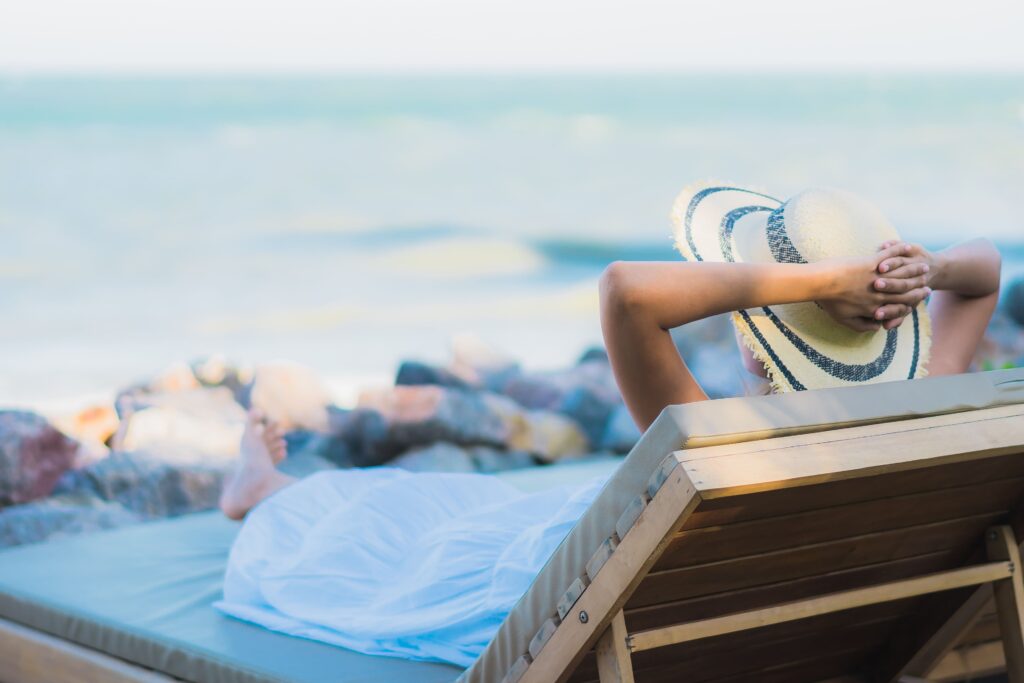Jeune femme se détendant sur une chaise longue sur la plage près de la mer, portant un chapeau de paille.
